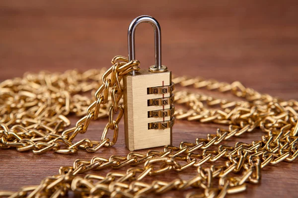 brass padlocks with a gold chain on a wooden background close up