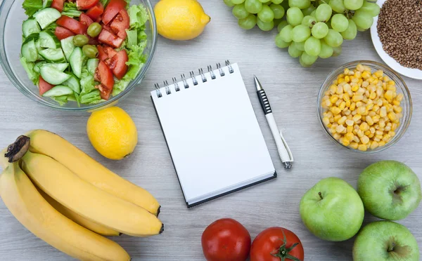 notebook with a diet plan with fresh vegetables and fruits on th