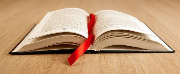 New open book on a wooden table with a red ribbon bookmark — Stock Photo, Image