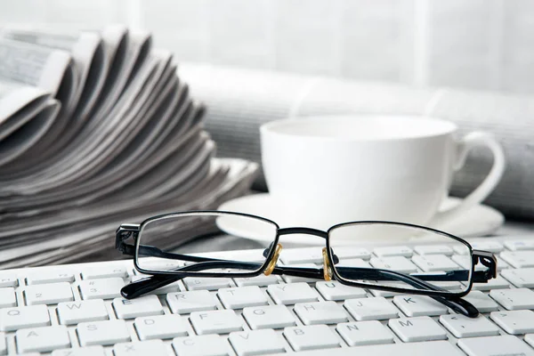 Brillen op het toetsenbord op kranten en een kopje koffie — Stockfoto