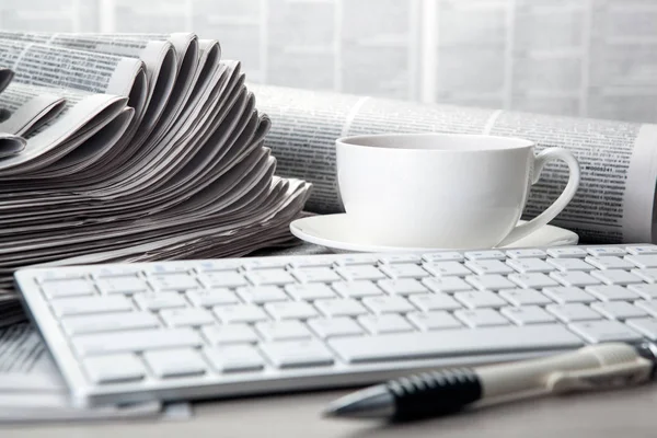 Tastiera sui giornali e una tazza di caffè sul tavolo — Foto Stock