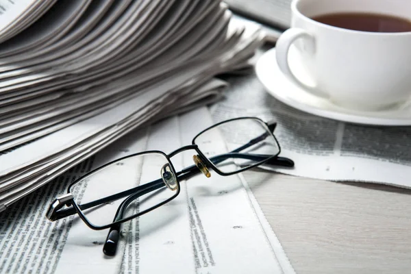Gazetelerde gözlük ve masada bir fincan kahve — Stok fotoğraf
