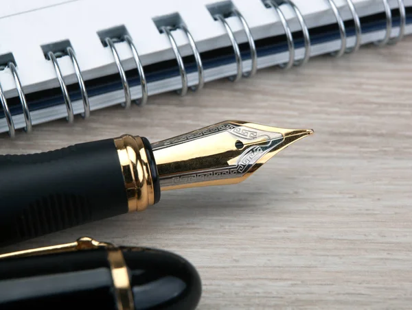 Gyllene fontän penna nära anteckningsblocket på ett träbord — Stockfoto