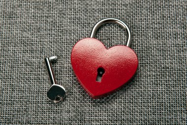 kalp şeklinde asma kilit ve gri keten üst görünümde bir anahtar.