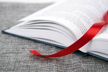 Gri bir masanın üzerinde kırmızı kurdeleli yeni bir kitap.