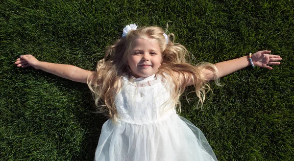 Маленькая Девочка Распущенными Волосами Белом Платье Лежит Зеленой Траве Вид — стоковое фото