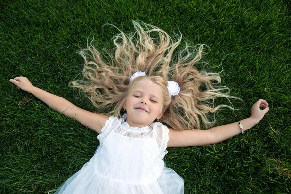 穿着白衣 头发蓬松的小女孩躺在绿草的顶上 — 图库照片