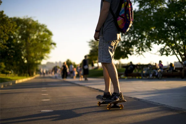 Şehir parkında kaykay süren genç bir adamın arka görüntüsü.