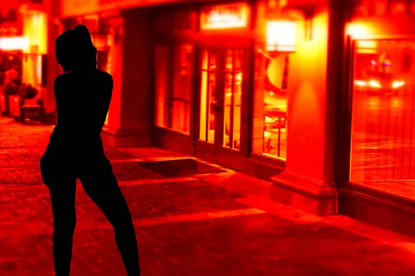 剪影的一个性感的年轻的胡克女孩站在街道上的红色窗口前 — 图库照片