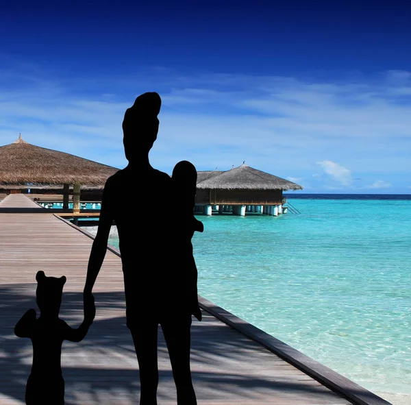 Family silhouette walking on the pier of a tropical resort at sea a mother with a little daughter holding hands and carrying a baby