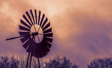 Eski model dekorasyon, günbatımında klasik paslı bir yel değirmeni, renkli gökyüzü ve bulutlar, tarımsal veya batı arka planı
