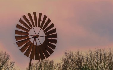 Günbatımında eski, paslı yel değirmeni, renkli gökyüzü ve bulutlar, tarım veya batı arka planı