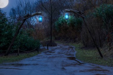 Gece yarısı çamurlu orman yolu. Tahta direklere asılı fenerler, fantezi ya da ürkütücü sahneler.