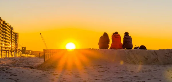 Tres adolescentes sentados en una colina de arena juntos, observando y disfrutando de la puesta de sol en la playa, jóvenes en la naturaleza — Foto de Stock