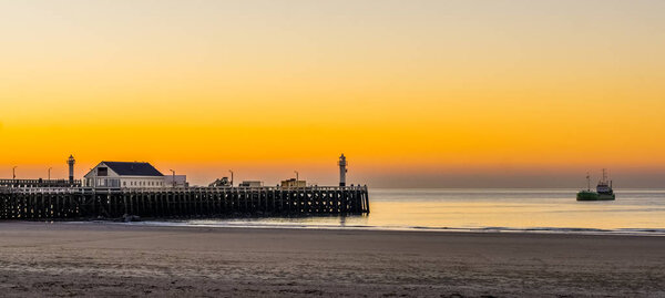 the harbor pier at the beach of blankenberge, Belgium, a boat sailing in the sea, beautiful sunset and colorful sky