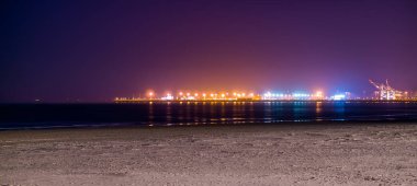 Blankenberge sahilinin kıyıları gece aydınlandı, uzaktaki sanayi bölgesinde renkli ışıklar yandı.