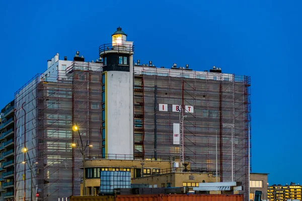 Verlichte vuurtoren met een gebouw in aanbouw op de achtergrond, architectuur aan de kust van Blankenberge, België, 15 februari, 2019 — Stockfoto