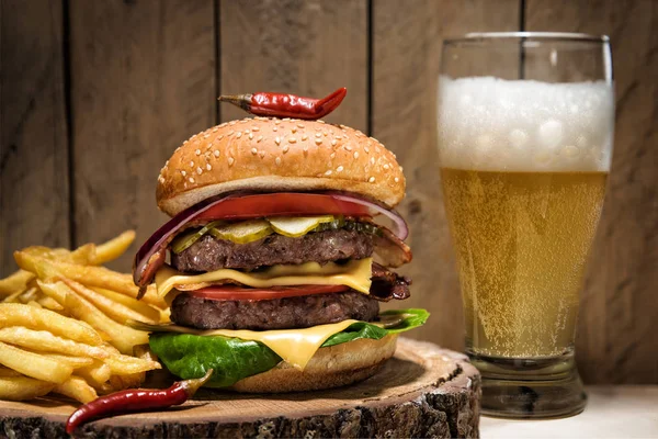 Grande cheeseburger con peperoncino, patatine fritte e un bicchiere di birra su fondo di legno . — Foto Stock