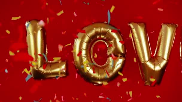 赤い背景に愛という言葉の黄金の大きな膨脹可能な文字 明るい色紙の紙吹雪が飛び回る バレンタインデー 招待状の結婚式 宣言の愛の創造的なおめでとうございます — ストック動画