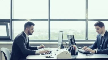 Şirket çalışanlarının bilgisayar monitörleri arkasında geniş parlak ofisinde çalışıyorum. Ofis çalışanı monitör ile perde arkasında. İş yerinde iş elbiseli iki genç işadamları. Büyük panoramik pencere.