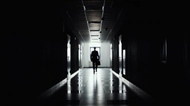 Kameraya doğru koridor boyunca güvenle yürüyen bir işadamı silüeti. Aydınlatma kontrol. İş yapmaya başla. Bir iş kariyerine başlamak.