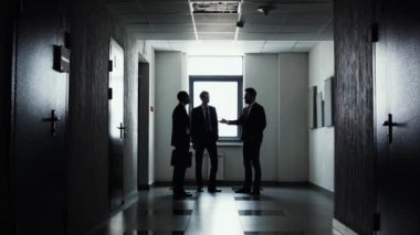 Üç iş adamları stending yönde ışık koridor boyunca siluetleri. Çalışma gün sonunda. Takım projesi üzerinde çalışmanın tamamlandı. İşadamı toplantıya gitmek.