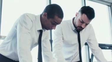 İki iş adamları, Kafkas ve masa ve proje, kağıtları çizelgeleri ile tartışmak bir Afrika Ulusal, stend gömlek içinde. İş takım çalışmalarını. Beyin fırtınası. Ofis panoramik pencerelere.