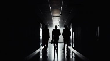 Siluetleri üç işadamlarından yönde ışık koridor boyunca yürüyüş. Çalışma gün sonunda. Takım projesi üzerinde çalışmanın tamamlandı. İşadamı toplantıya gitmek.
