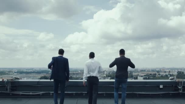 三商人 两个白人和一个非洲国家 来到摩天大楼的屋顶边缘 在屋顶边缘的商人看着这个城市 享受着成功 顶级业务 — 图库视频影像