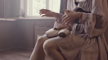 Balerin pointe ayakkabı onun elinde tutan, bale terlik şeritler unravels. Dans için hazırlayın. Bir iç stüdyo panoramik pencerelere ile eski tarzda. Haze ile doğal aydınlatma.