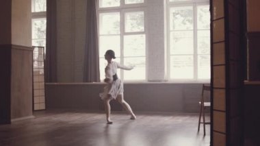 Balerin dans içinde atlama yapar ve sicim uzanır. Bale dans. Balerin havadar bir güzel zarif elbise ve Bale terlik yavaşça eski bir iç Studio büyük pencereler ile dans ediyor.
