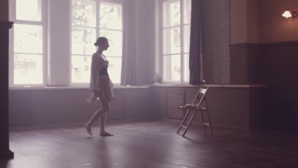 芭蕾舞演员穿着漂亮的浅色连衣裙 手里拿着鞋 准备舞会吧一个室内工作室在旧的风格与全景窗口 自然照明与薄雾 — 图库视频影像