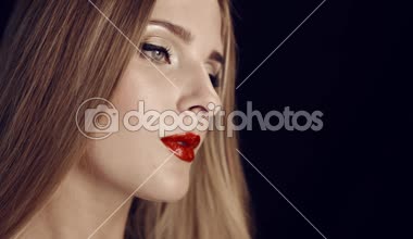 Güzel yüzünü bir genç kızın stüdyoda siyah bir zemin üzerine kırmızı dudaklar profesyonel makyajlı. Kameraya bakar ve uzak görünüyor. Akşam makyaj, samimi ortamı.