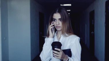 Bir fincan kahve ve belgeler ile genç iş kadını Smartphone'da konuşuyor.