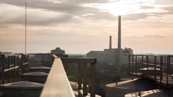 工業都市を背景にした夕焼け 工場の屋根からの写真 雲の中の日の出を背景にパイプ工場と都市のパノラマ — ストック動画