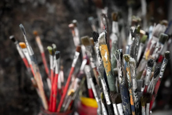 A lot dirty artist paint brushes in a bucket. Different artist brushes, close-up view