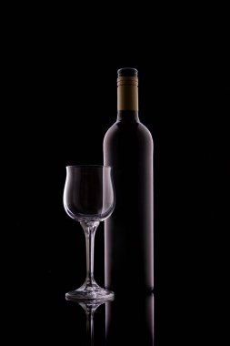 Boş şeffaf cam ve şişe ile siyah bir zemin üzerinde kırmızı şarap ve yansıtıcı yüzey yan ve arka ışıklandırma.