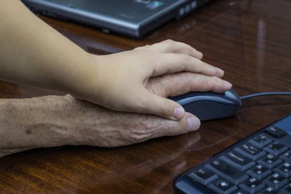 Bir bilgisayar fare kullanan yaşlı bir adamın elini bir çocuğun el denetler.