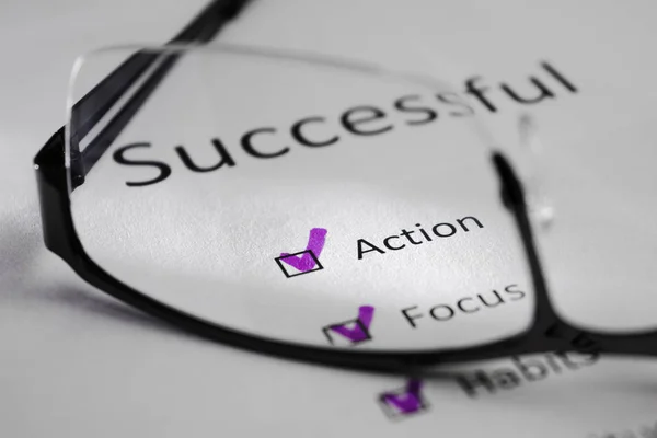 ACTION inscription on a white sheet. This is a motivational checklist with points for success. Opposite the lines there are check marks in black squares. The picture was taken through the lens of glasses and highlighted by a beam of light.