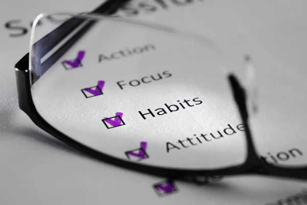 Beyaz bir levha üzerinde alışkanlıkları yazıt. Bu bir motivasyon kontrol listesi ile başarı için puan var. Satırları siyah kareler onay işaretleri vardır. Resmi gözlük lens ile çekilen ve bir ışık huzmesi tarafından vurgulanan.