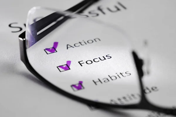 FOCUS inscription on a white sheet. This is a motivational checklist with points for success. Opposite the lines there are check marks in black squares. The picture was taken through the lens of glasses and highlighted by a beam of light.