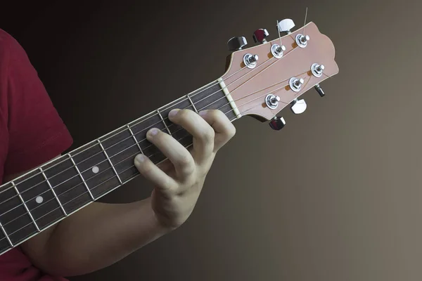 若いギタリスト アコースティック ギターの首の上の左の手のクローズ アップ 茶色の背景に撮影した写真 — ストック写真