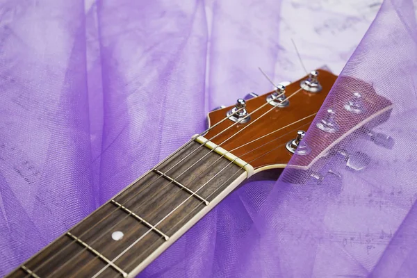 紫の透過的なファブリックのひだにあるアコースティック ギターのクローズ アップ — ストック写真