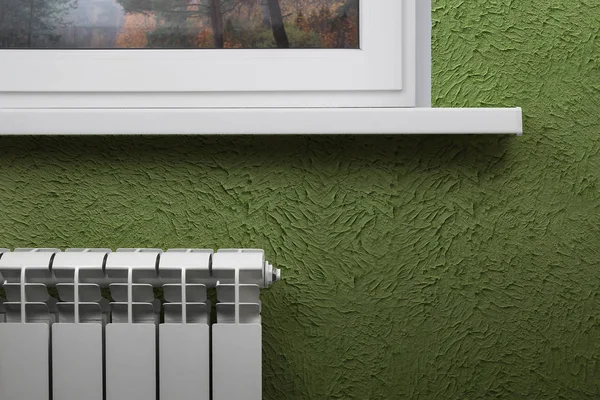 Beyaz Seksiyonel radyatör arka planda bir beyaz pencere altında yeşil bir duvar Isıtma. Görüntü yazıt için boş bir alana sahip.