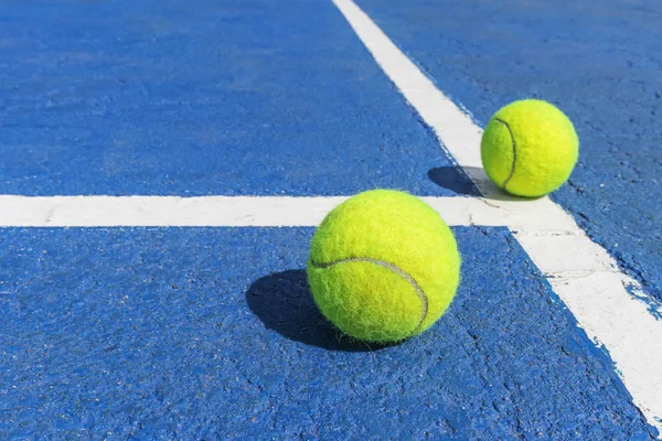 Two tennis balls on a blue tennis court with white marking lines