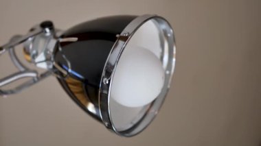 Bir masa lambası yanar. Ampul daha aydınlık olur. Arka planda, bir whitae duvar.