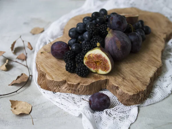 Blue and purple food. Blackberries, grapes, plums, blueberries, figs on a wooden background. Tasty and ripe fruits and berries. Autumn arrangement of fruits. Copy space, close up