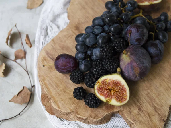 Blue and purple food. Blackberries, grapes, plums, blueberries, figs on a wooden background. Tasty and ripe fruits and berries. Autumn arrangement of fruits. Copy space, close up, top view