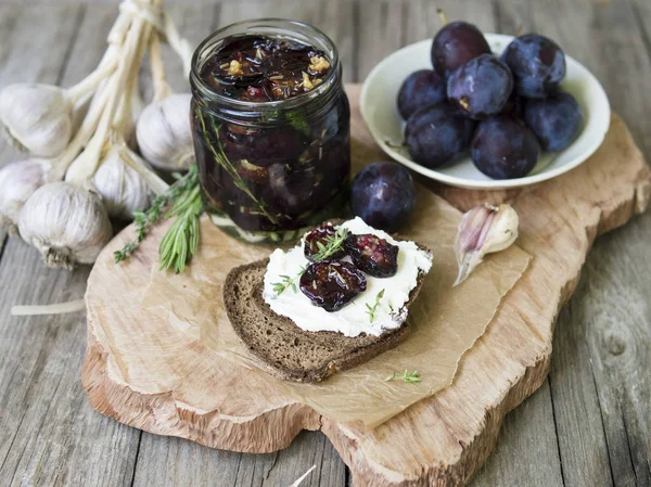 Glass jar with dried plums and fresh rosemary on wooden serving board, selective focus.