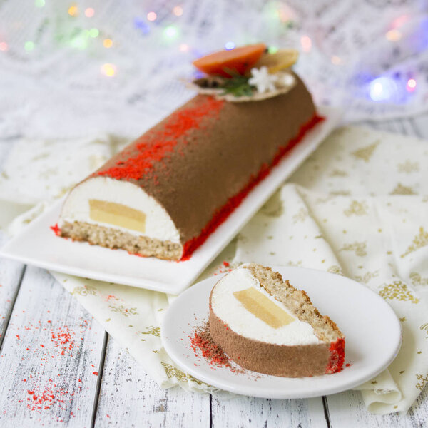 Chocolate yule log christmas cake, also know as Buche de Noel, with tangerine mousse decorated with persimmon, orange chips, star aniseas on wooden background. Праздничная атмосфера, настроение. Новый год
